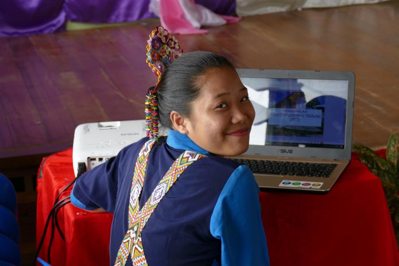 Junge Frau in traditionellem Runge-Schmuck mit Laptop & Beamer.