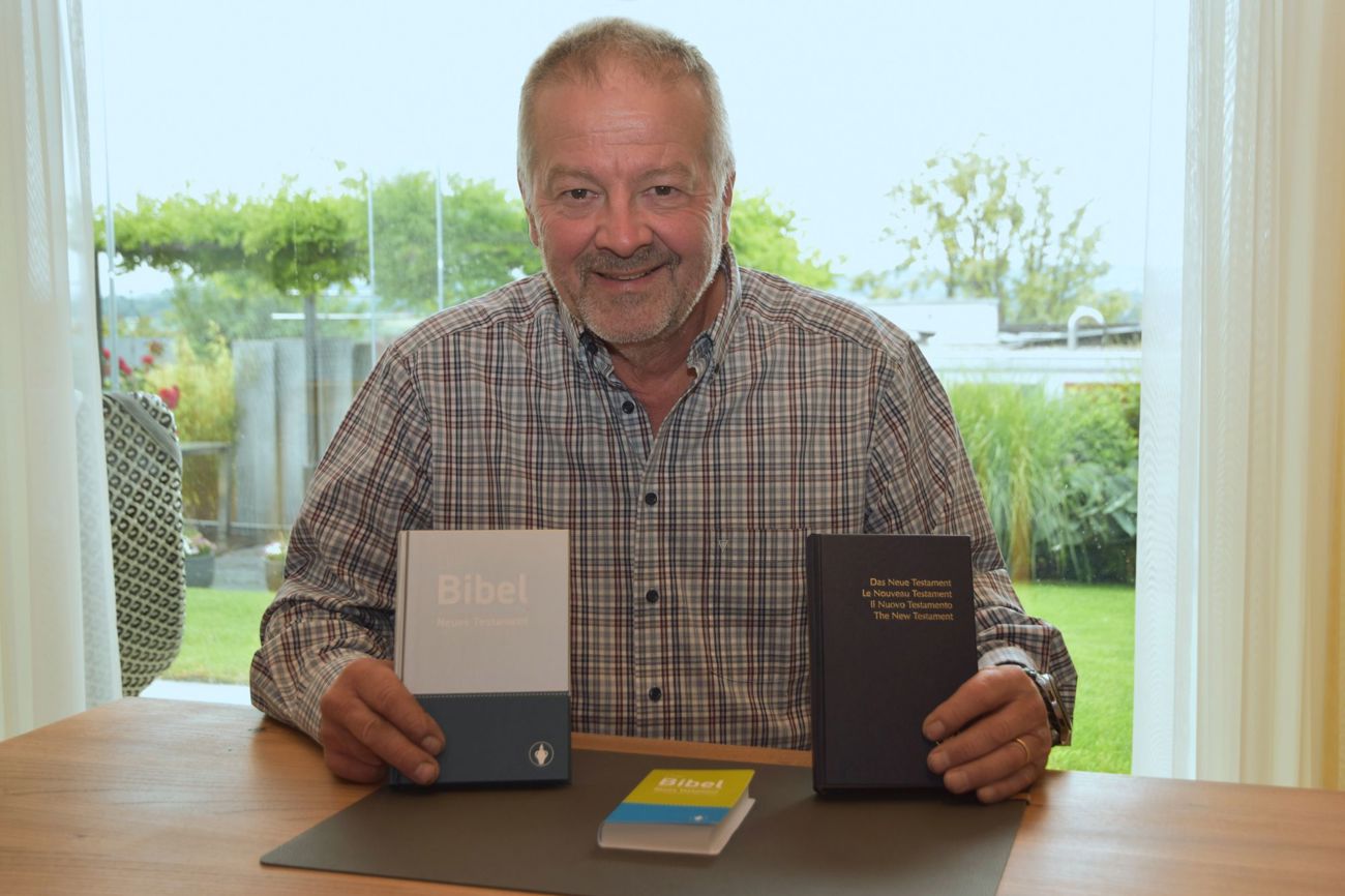 Fredy Baumann zeigt die drei Bibelformate (von links nach rechts): die Bibel mit Grossdruck, diejenige im Taschenformat und die viersprachige Ausgabe. (Bild: Kim Ariffin)